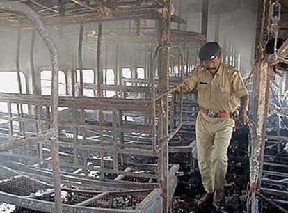 Un policía camina entre los restos de uno de los vagones incendiados por manifestantes en Godhra (India).