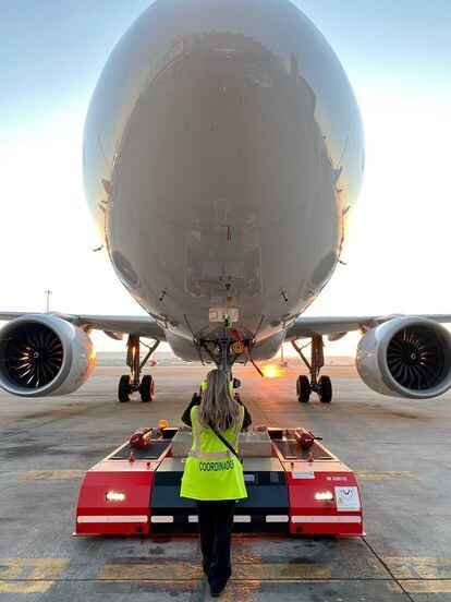 Una operaria de Iberia dirige el movimiento de un avión a través de un remolcador o tractor de pushback.