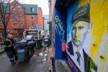 A man picks up trash from a Toronto alley in front of a portrait of Vladimir Putin on Monday.