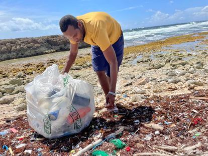 Un voluntario de Green Phenix recoge plásticos que la marea ha traido a la costa, en una playa de Curaçao.