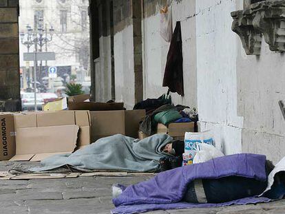 Varias personas sin hogar protegiéndose del frío con cartones y mantas en pleno centro de Bilbao.