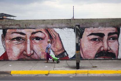 Una mujer pasa frente a un muro con una pintada de Ch&aacute;vez y Maduro.