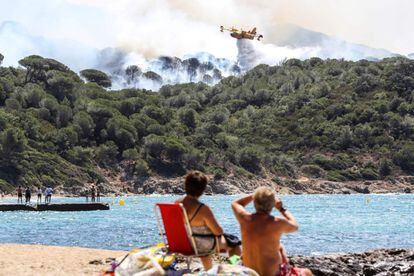 Dos personas observan, desde la playa, un avión contraincendios trabajando en las tareas de extinción de un fuego declarado en La Croix-Valmer, cerca de Saint-Tropez (Francia).
