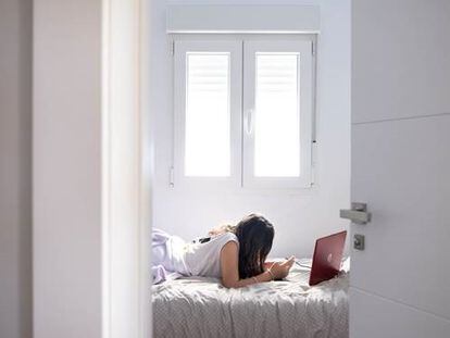 Una joven mira su ordenador y móvil en su habitación.