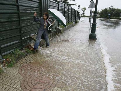 Una mujer intenta cruzar una acera en Vigo, inundada a consecuencia de las fuertes lluvias.