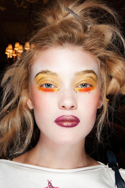 Más baño de exceso, como no podía ser de otra manera, de la mano de Vivienne Westwood. Labios en berenjena con destellos dorados y ojos amarillos y naranjas: un look tan maravilloso como imposible.