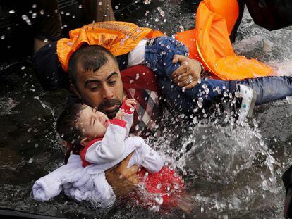Un refugiado sirio coge a un ni&ntilde;o en su llegada a la isla griega de Lesbos.