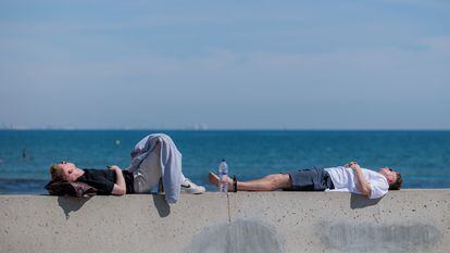 Dos jóvenes descansan al sol en la playa de la Malvarrosa, en Valencia.