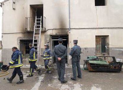 Bomberos y guardias civiles ante la puerta de la casa incendiada en Cuenca donde han muerto dos ancianos.