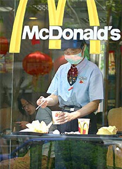Una empleada de un restaurante de comida rápida sirve las mesas protegida con una mascarilla, como ordenan las autoridades chinas.