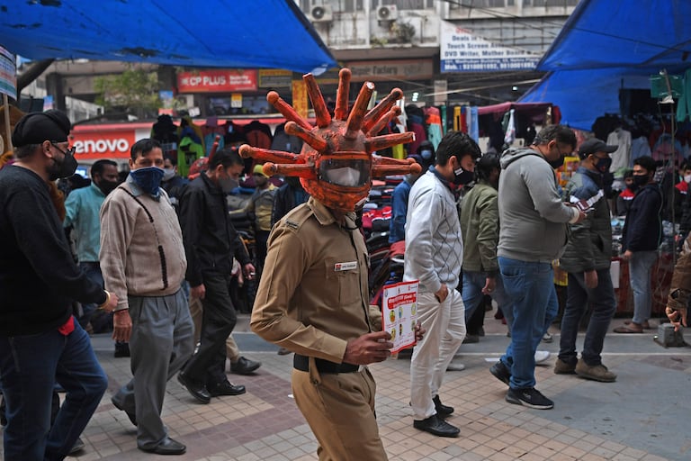Un voluntario de defensa civil pasea por un mercado en Nueva Delhi, con un casco anticovid y un panfleto con información, como parte de una campaña de concienciación en La India.