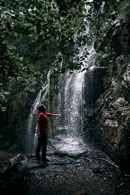 2KF2HKW latin girl with left arm outstretched and palm up wet by waterfall water, guanga waterfalls, spain