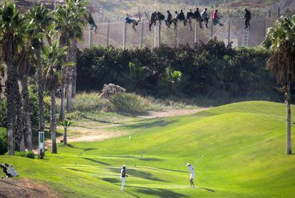 Al menos 12 inmigrantes, encaramados en la valla de Melilla frente al campo de golf situado al lado de la alambrada que separa la ciudad autonoma de Marruecos. 
