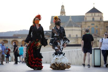 Dos mujeres protegidas con máscaras sanitarias y vestidas de flamencas dan un paseo por las calles de Córdoba, este viernes.