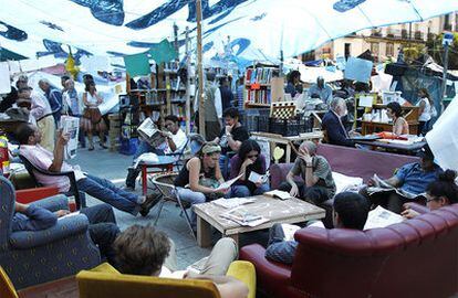 Varias personas leen la prensa en la biblioteca de los acampados en Sol.