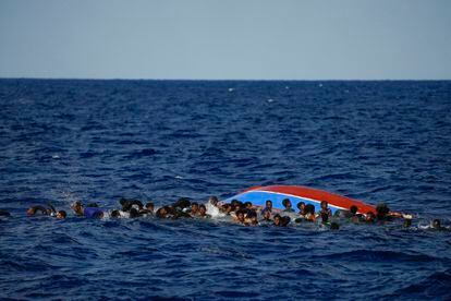 Los migrantes permanecen junto a la embarcación volcada a la espera de ser auxiliados.