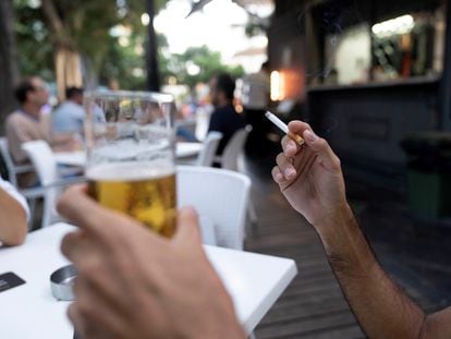 Una persona sostiene un cigarrillo en la terraza de un bar.