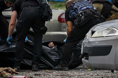 Ukrainian policemen carry the body of a person killed by the Russian attack.