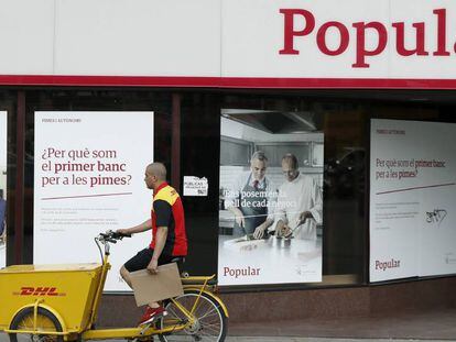 Un repartidor pasa por delante de una oficina del Banco Popular, en Barcelona.