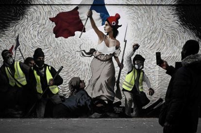 Un hombre toma una fotografía de un mural del artista callejero PBOY que muestra a los manifestantes de los chalecos amarillos (gilets jaunes) inspirados en la pintura de 'La Liberte guidant le Peupl', en París, el 8 de enero de 2019.
