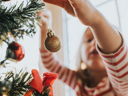 Una niña decora un árbol de Navidad.