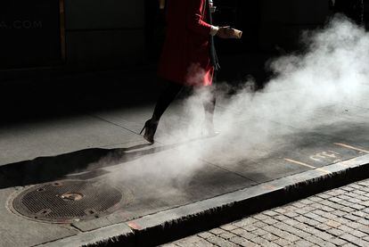 Una mujer camina frente a la Bolsa de Nueva York mientras sale vapor por una alcantarilla.
