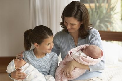 Imagen familiar en la que una niña con un muñeco imita el rol de su madre con el bebé.