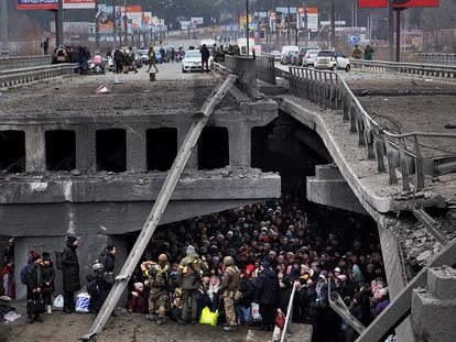 Ucranios intentan pasar por debajo de un puente destruido en Irpin, cerca de Kiev, este sábado.