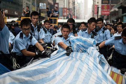 El procedimiento transcurrió sin problemas pero en un momento dado numerosos manifestantes comenzaron a plantar cara a los agentes y a reclamar poder desmontar ellos mismos un escenario que había sido instalado en la zona. En la imagen, la policía retira una lona de la zona tomada por los manifestantes prodemocracia en el centro de Hong Kong.
