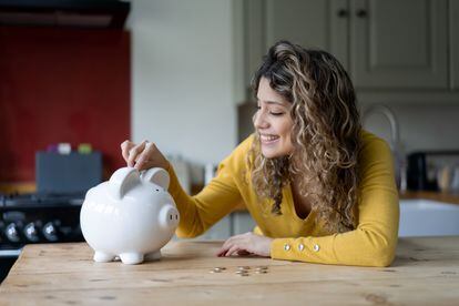 Cheerful young woman saving coins in her piggy bank smiling.