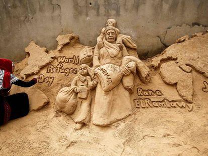 La escultora de arena palestina Rana Ramlawi finaliza una nueva creación artística que conmemora el Día Mundial de los Refugiados en la ciudad de Gaza el 20 de junio de 2020. Su obra representa a una mujer que lleva a una niña niña de la mano y un saco de harina con el logotipo de la Agencia de Obras Públicas y Socorro de las Naciones Unidas para los Refugiados de Palestina (UNRWA) y también un niño sobre sus hombros sosteniendo un bidón de agua, ante un mapa del mundo.