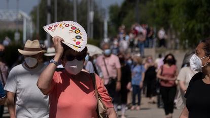 Una mujer se protege del sol y el calor con un abanico en la cola que da acceso al centro de vacunación instalado en el Estadio Olímpico de Sevilla.