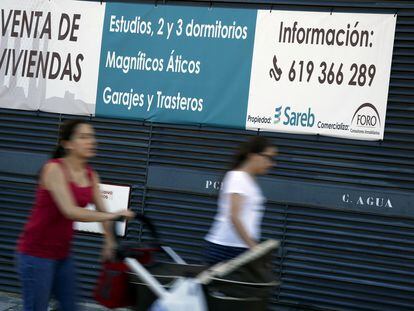 FILE PHOTO: People walk past signs advertising apartments for sale outside a Sareb owned building in Madrid March 31, 2015. REUTERS/Susana Vera/File Photo