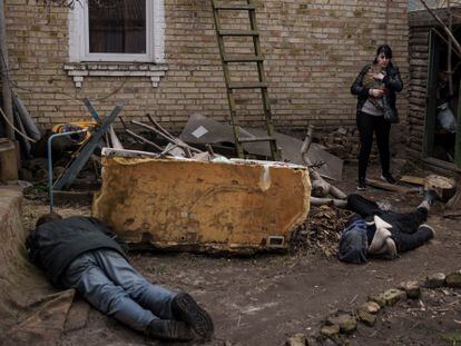 Una mujer pasa frente a varios cadáveres a las puerta de su casa en Bucha (Ucrania).