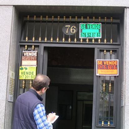 Un hombre observa unos carteles de "Se vende" a la entrada de un edificio