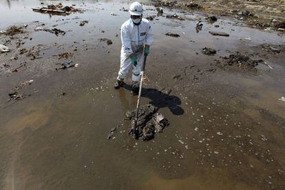 Un policía, con un traje antirradiación, busca cadáveres en el lodo cerca de Fukushima.