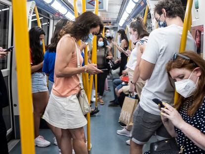 Un grupo de personas consulta sus teléfonos móviles en un vagón del metro de Madrid.