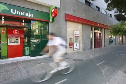 Un ciclista pasa ante una sede de Unicaja y Cajasur en Sevilla.