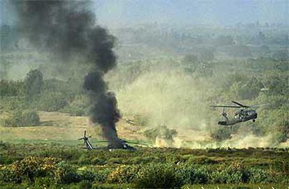 El helicóptero norteamericano atacado en Tikrit arde en tierra, envuelto en una humareda, mientras otro aparato transporta a los heridos.