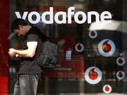 Un hombre consulta su tel&eacute;fono junto a una tienda de Vodafone.