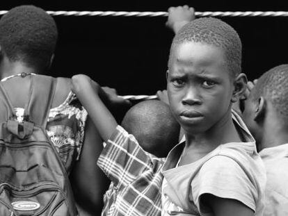 Una niño espera a entrar a la escuela en el campamento de Nyumanzi mientras mira a sus otros compañeros por la ventana del aula.