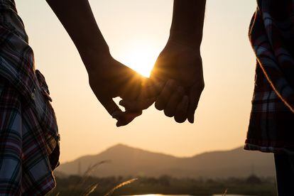 Close up of loving couple holding hands while walking at sunrise sunset in the meadow mountain in background. Valentine&#8217;s Day and love concept.