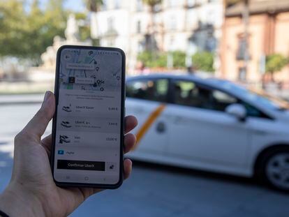 Imagen de un móvil con la app de Uber y un taxi de fondo, el día en que se aprobará el decreto para regular las VTC en Andalucía (septiembre de 2022).