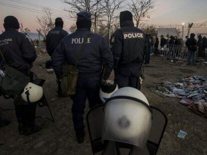 Varios polic&iacute;as vigilan a un grupo de refugiados en Grecia.