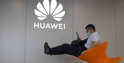 Un hombre consulta su móvil junto a un logo de Huawei. 