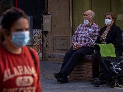 Dos personas mayores protegidas con mascarillas descansan sobre un banco en el barrio de Triana de Sevilla.