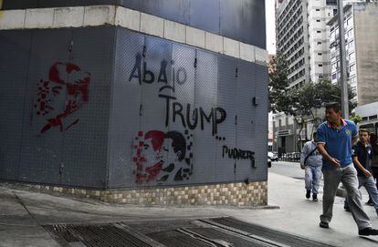Una persona camina cerca de un grafiti que retrata al expresidente venezolano Hugo Chávez y al presidente Nicolás Maduro, acompañados del texto "Abajo Trump".