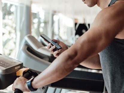 Una persona mira su teléfono móvil mientras utiliza una cinta de correr.