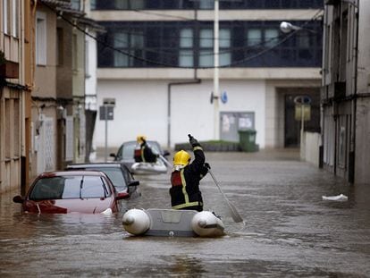 El temporal de lluvia anega pueblos y obliga a rescatar familias en Galicia. Dos bomberos atraviesan en lanchas una calle de Sada.