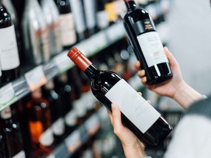 Una mujer elige botellas de vino tinto del estante de un supermercado.